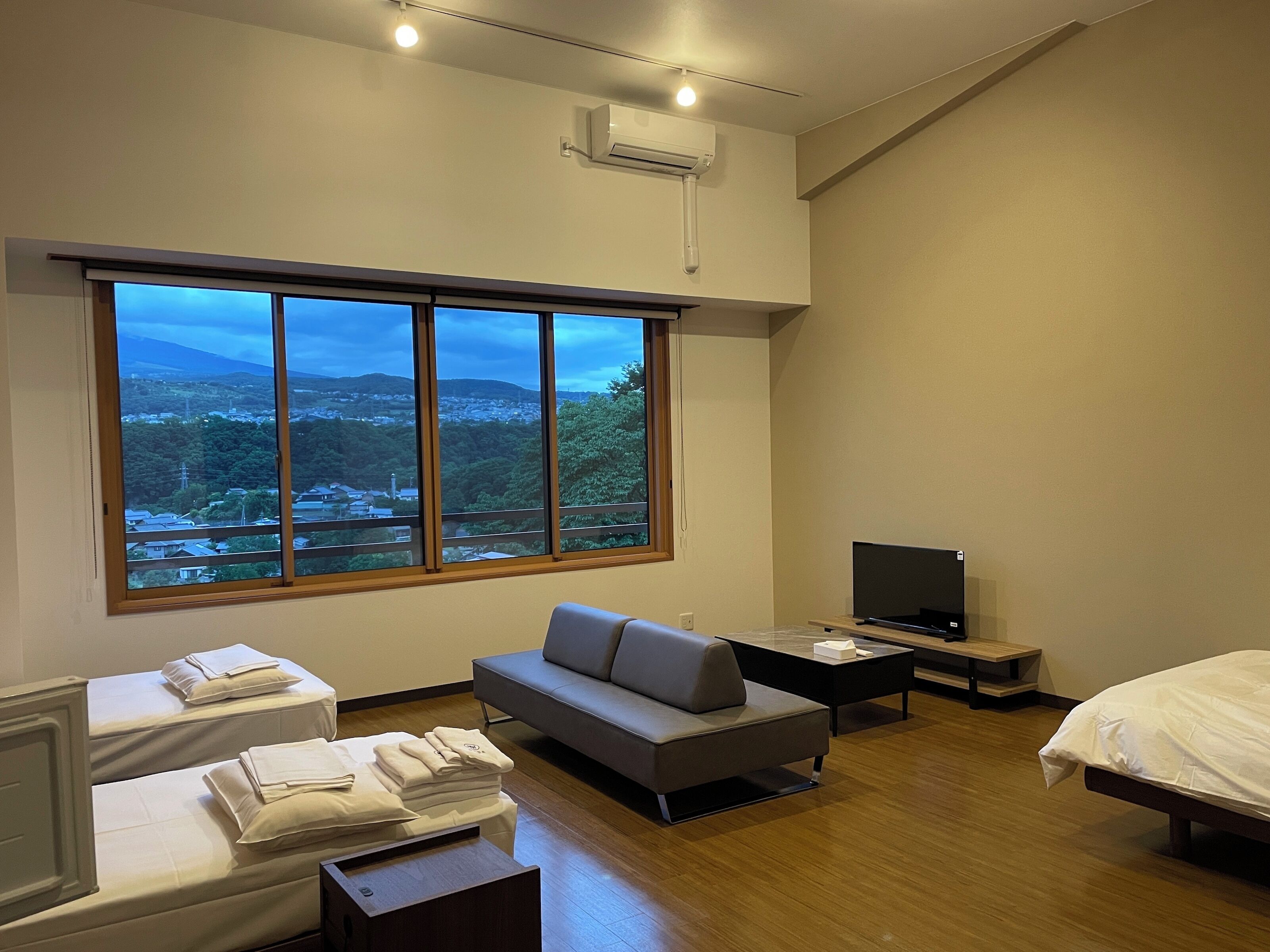 A modern hotel room with a large window, a sofa, a bed, a TV, and a desk.