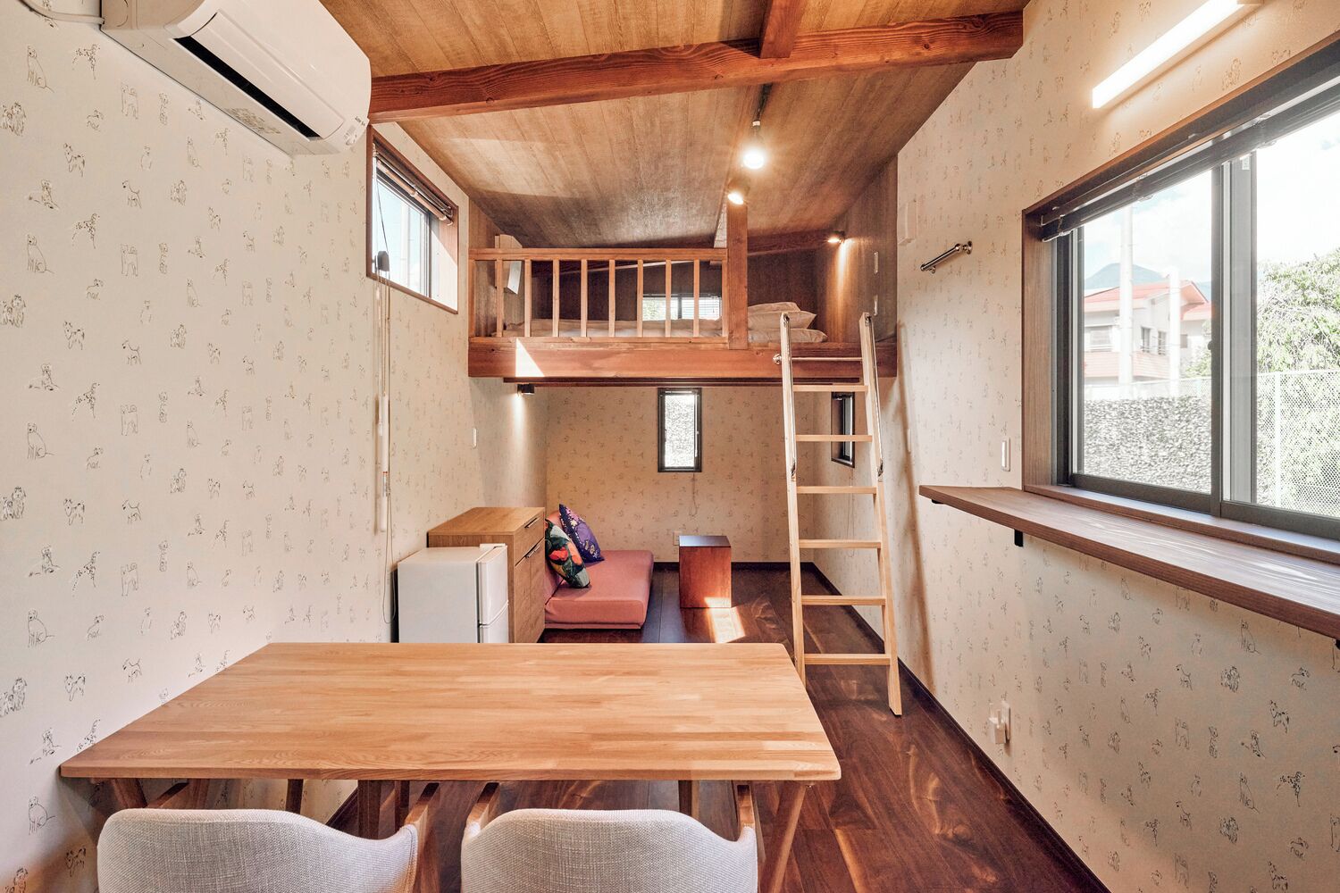 A compact room with a wooden table, two chairs, a bunk bed, and a ladder.