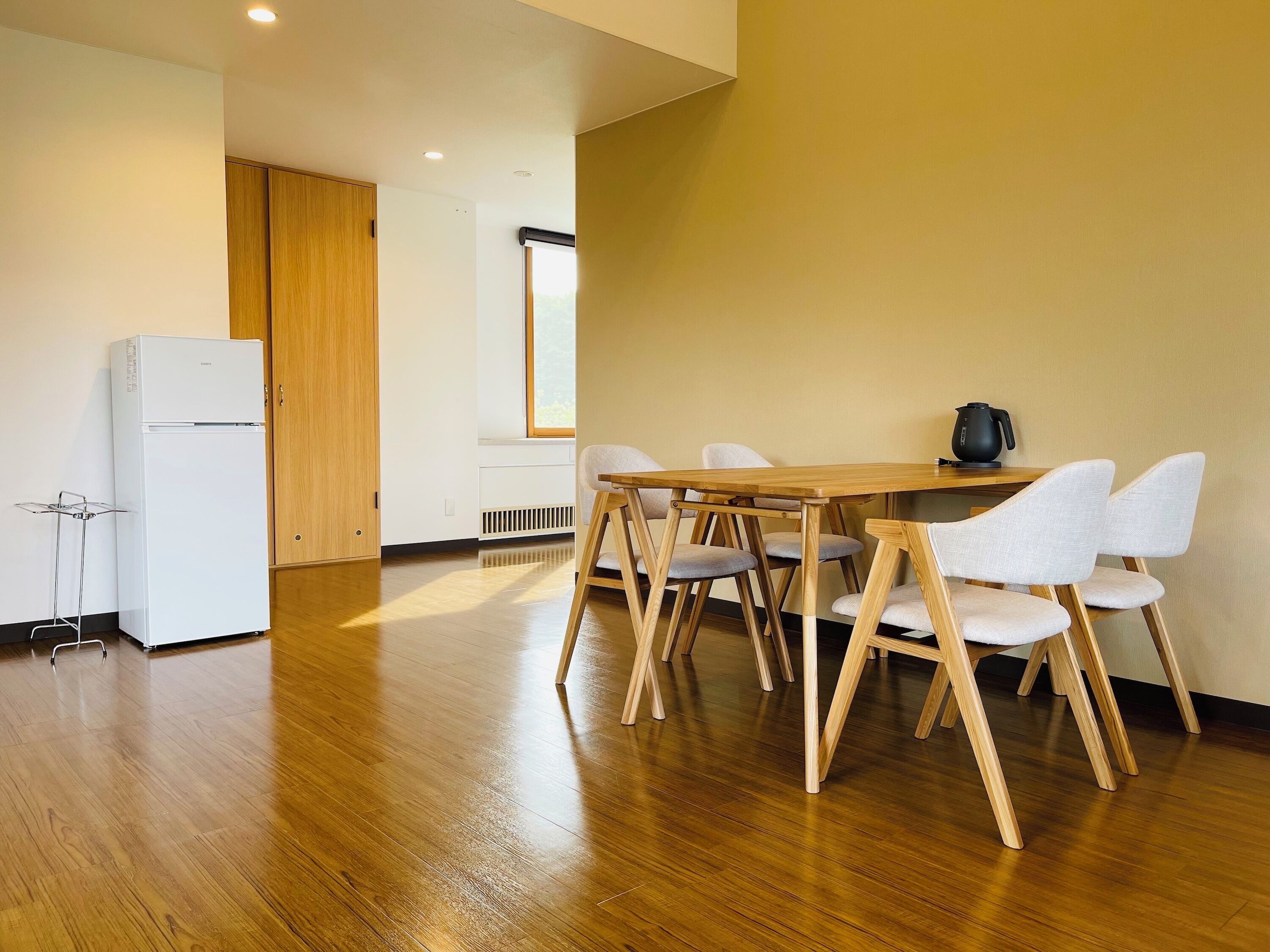 Une cuisine moderne avec un réfrigérateur blanc, des armoires en bois et un coin repas comprenant une table en bois et quatre chaises.