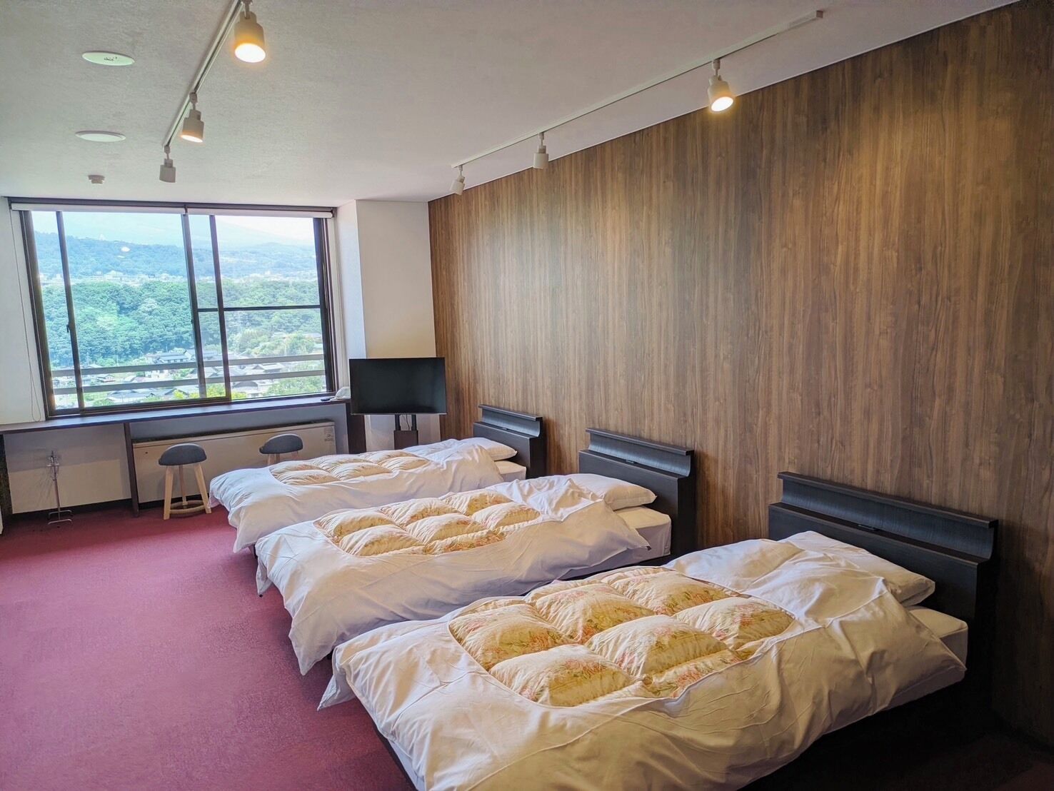 A hotel room with two beds, a large window with a view, a desk, and a chair.