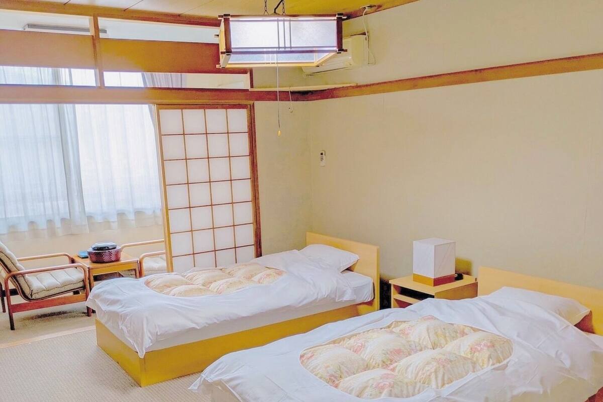 Une chambre d’hôtel avec deux lits, un coin salon comprenant une chaise et une table, et une grande fenêtre donnant sur un beau paysage.