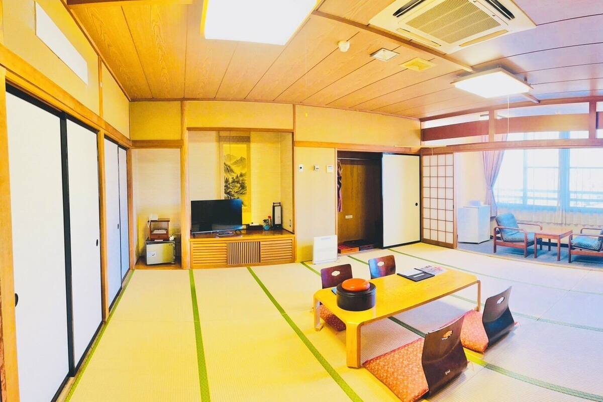 Une pièce de style japonais traditionnel, avec un sol recouvert de tatamis, une table basse avec des coussins, un téléviseur et des portes coulissantes.