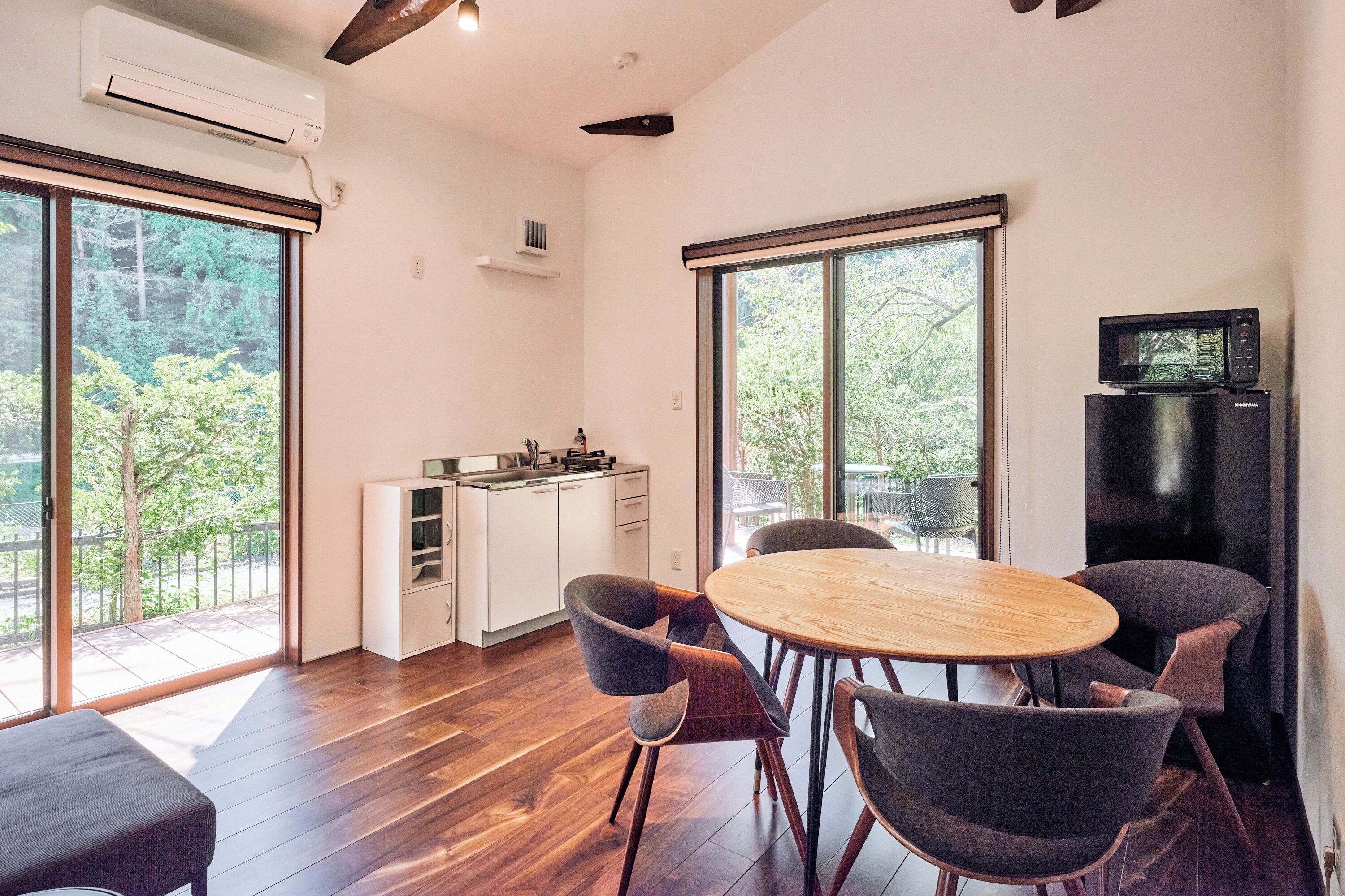 A modern kitchen with a built-in stove, a dining area with a round wooden table and four chairs, and large windows offering a view of greenery.