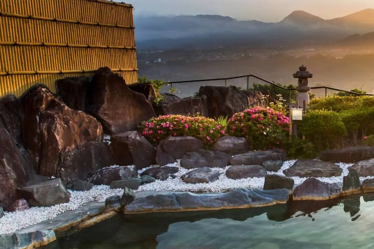 A serene outdoor pool area with rocks and pebbles, surrounded by lush greenery and a bamboo fence.