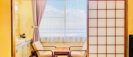 Una tradizionale stanza giapponese con pavimento in tatami, un paravento shoji, un tavolino, due sedie e un lavandino con articoli da toilette.