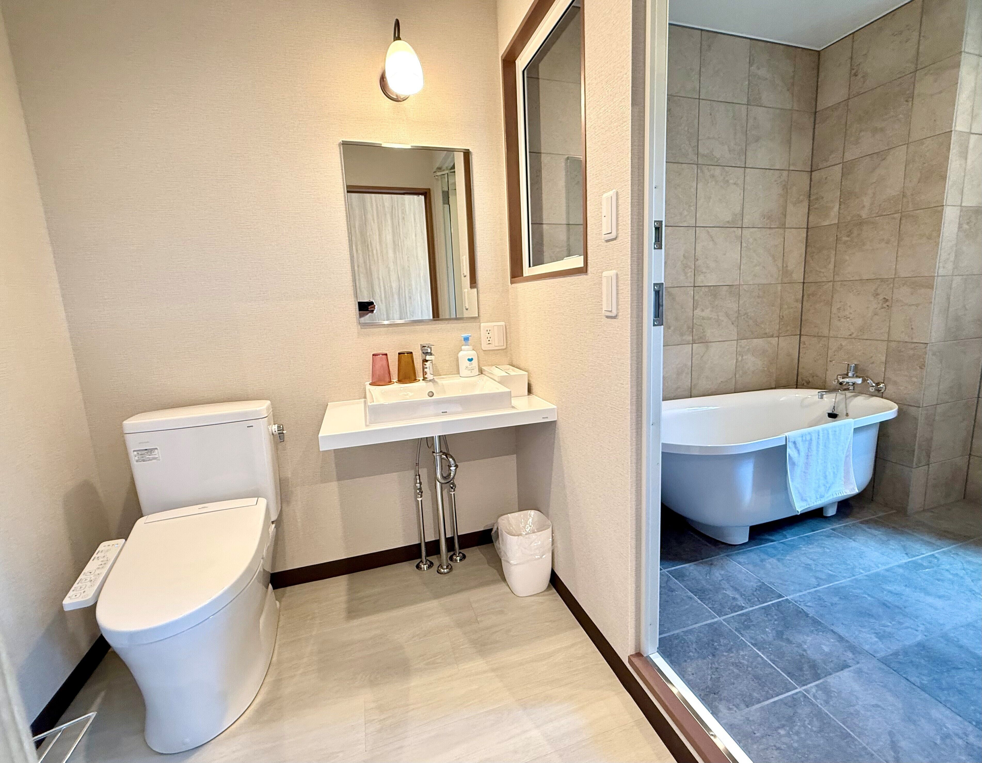 A modern bathroom with a toilet, sink, mirror, and bathtub.