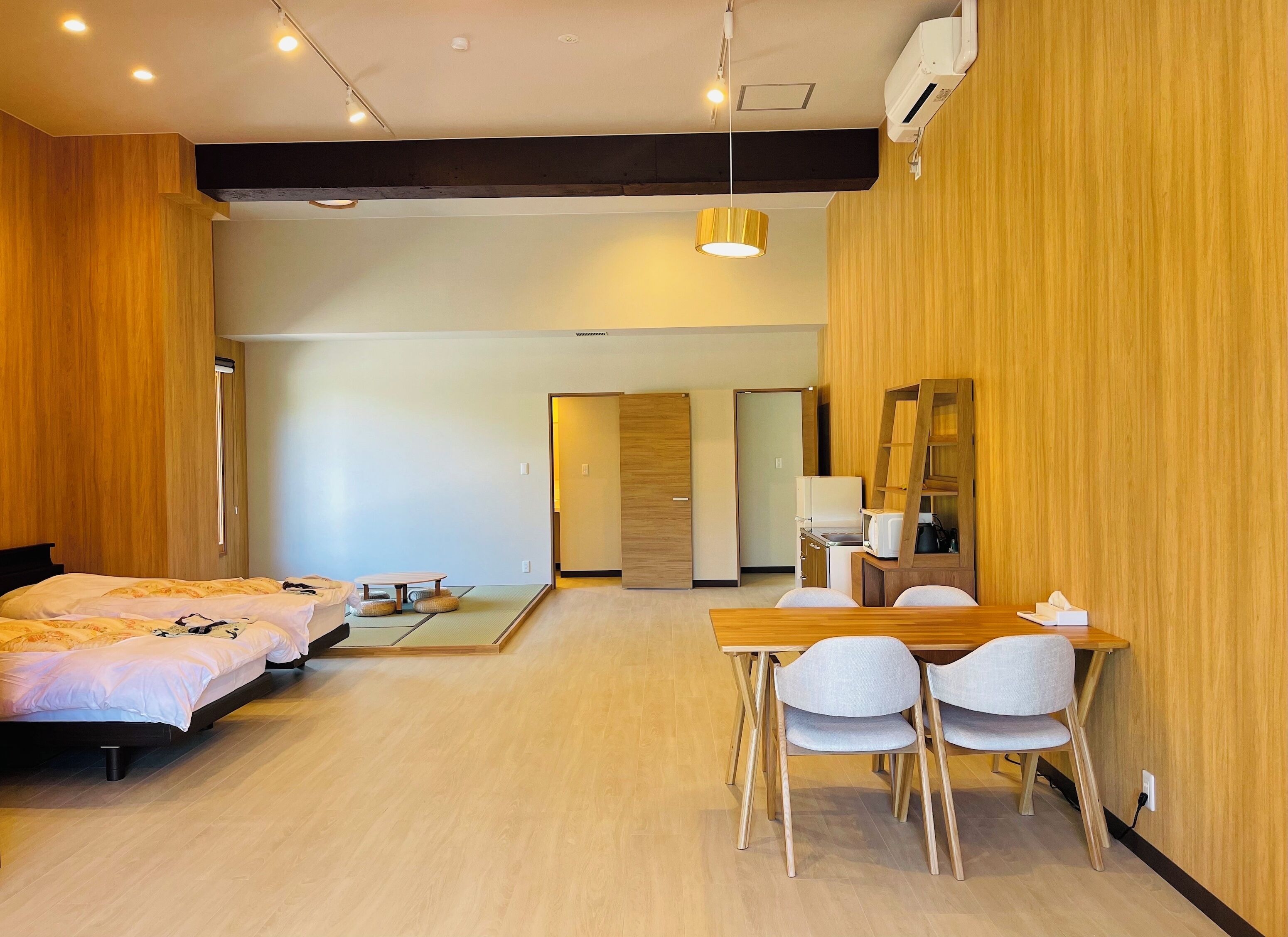 A hotel room with two beds, a dining table with chairs, a small table with a lamp, and a mirror on the wall.