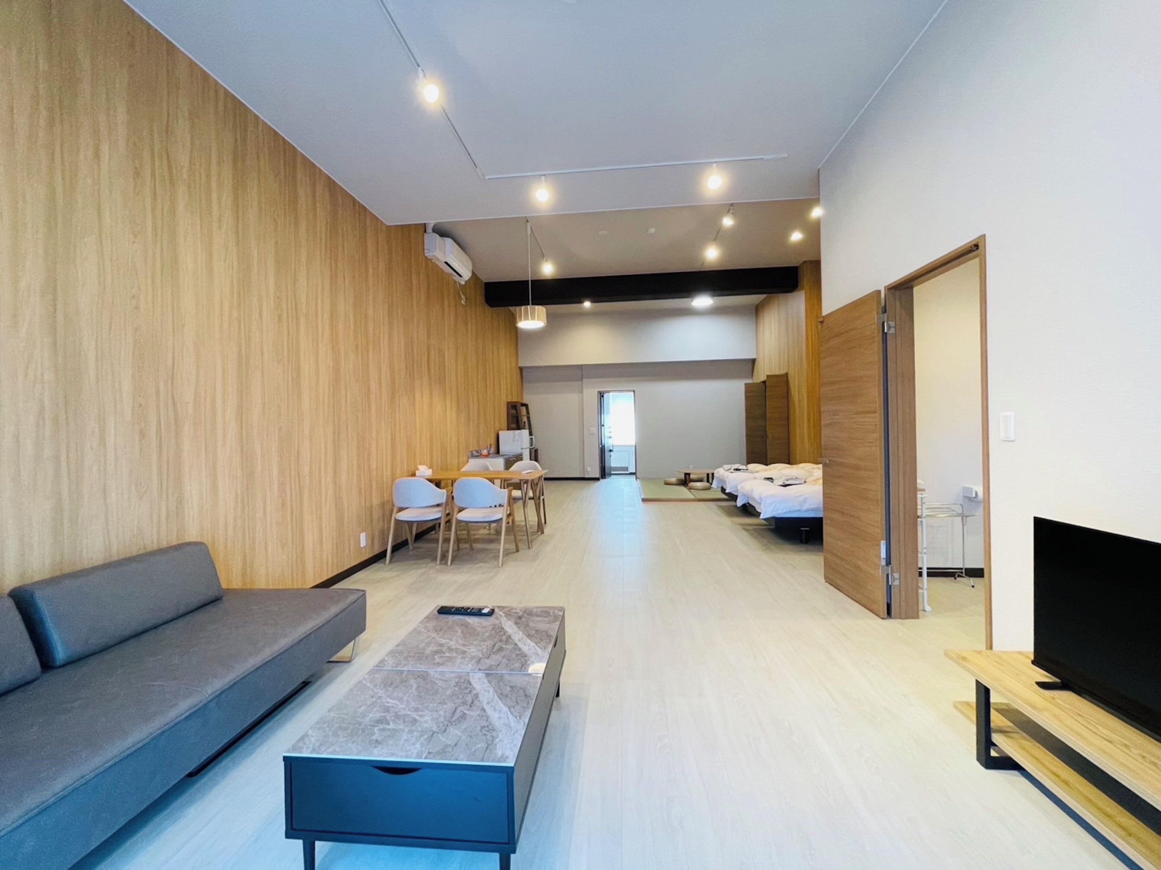 Una habitación de hotel moderna con sofá, una mesita, televisor y cama con cabecero de madera.