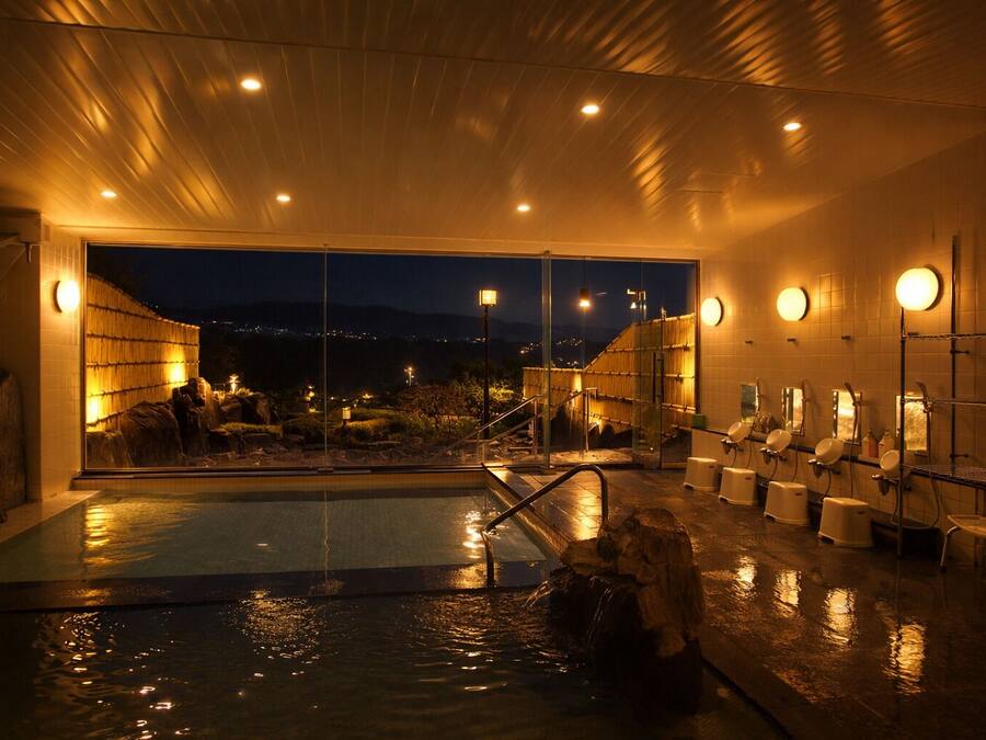 Piscina coberta aquecida com vista para o céu noturno, cercada por áreas de estar e uma parede de bambu.