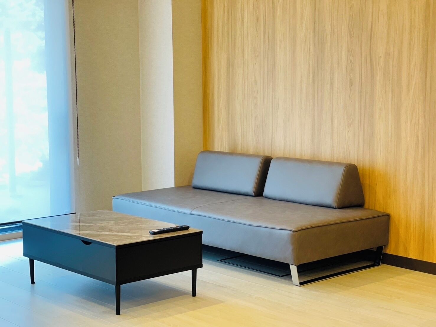 A modern living room with a sofa, a glass coffee table, and a remote control on it.