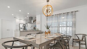 Une cuisine moderne avec des meubles blancs, un îlot central doté de sièges et un lustre.