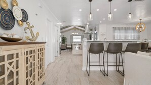 Une cuisine moderne dotée d’un îlot central, de tabourets de bar, de luminaires suspendus et d’assiettes décoratives accrochées au mur.