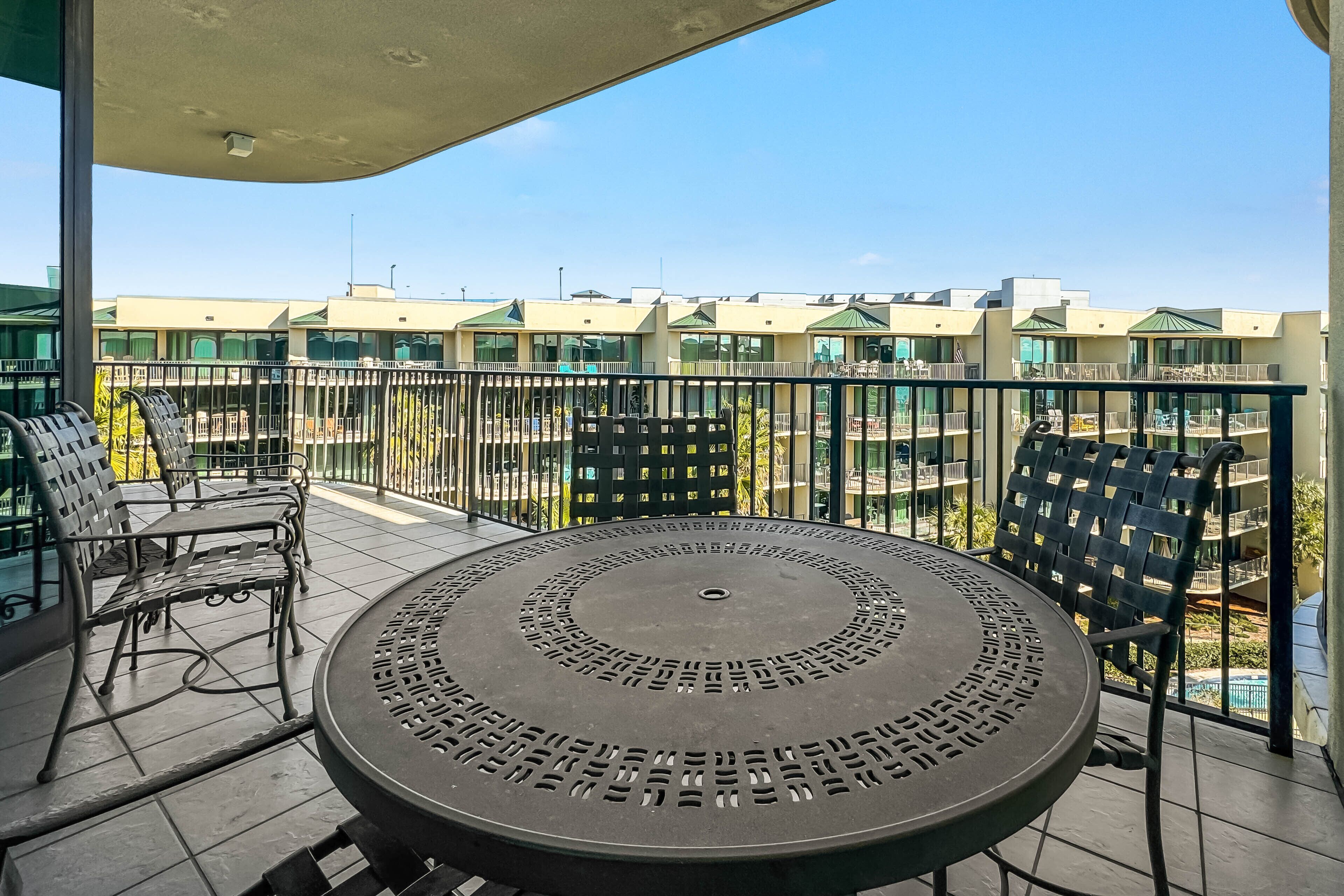A balcony with a round table and chairs, a view of other buildings, and a clear sky.