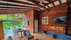 A log cabin with a pool, outdoor seating, and a TV on the wall. - Charming 3-bedroom beach cabin with Starlink WiFi, AC in enchanting Tamanique (Tamanique)