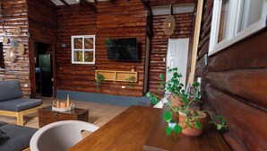 A wooden cabin interior with a wooden dining table, a sofa, a TV mounted on the wall, and potted plants. - Charming 3-bedroom beach cabin with Starlink WiFi, AC in enchanting Tamanique (Tamanique)