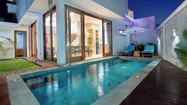 A modern house with a swimming pool, a patio with lounge chairs, and a well-lit interior.