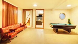 A room with a pool table, a sofa, and a staircase leading to an upper level.