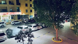 A parking lot with several cars, a grocery store, and a tree in the foreground. - Amazing 3-bedroom apartment with WiFi in Ajman (Ajman)