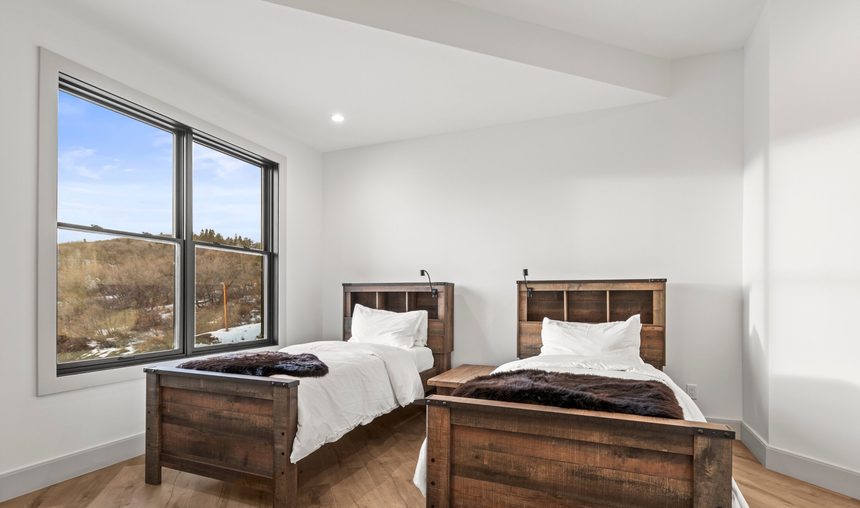 A bedroom with two wooden beds, a large window with a view of a snowy landscape, and a white ceiling.