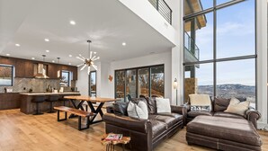 A spacious living area with a large window offering a mountain view, a wooden dining table, and a leather sofa.