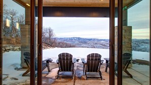 A patio with two Adirondack chairs facing a snowy landscape with mountains in the background.