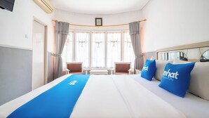 Ein Hotelzimmer mit einem großen Bett, zwei Sesseln, einem kleinen Tisch und einem Fenster mit Vorhängen.