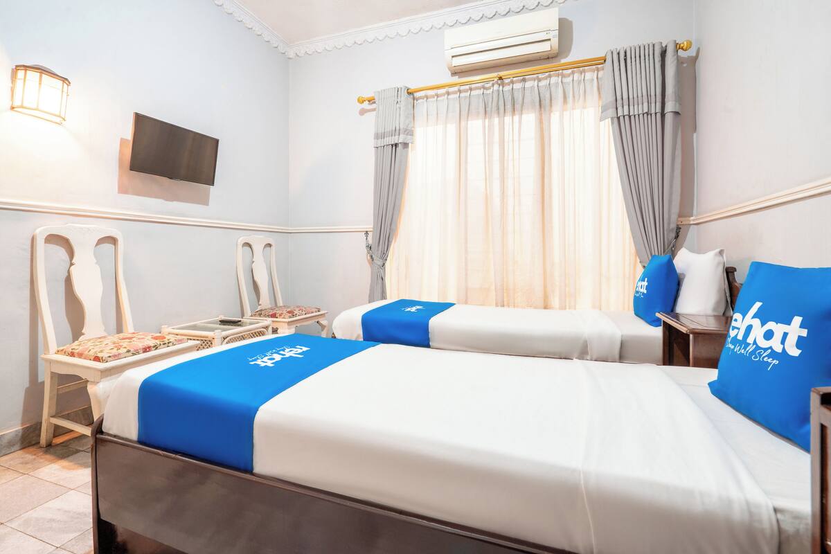 Ein Hotelzimmer mit zwei Betten, einem Fernseher, einem Schreibtisch und einem Sessel.