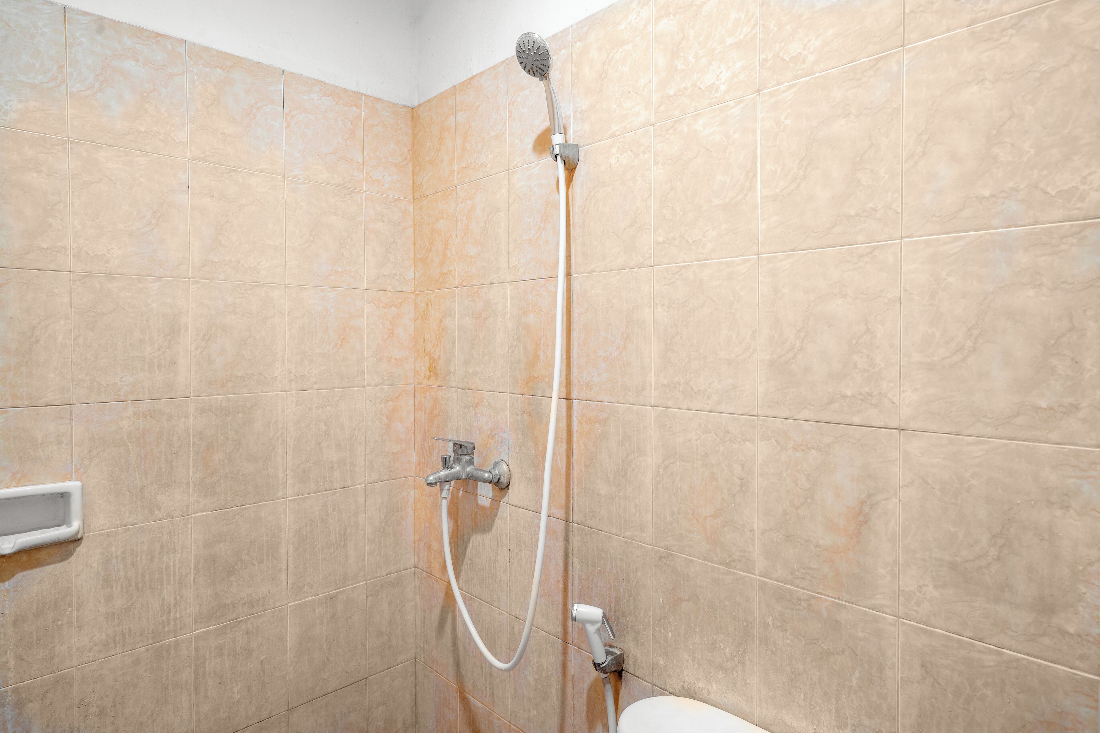 Une salle de bain avec des carreaux de couleur beige, une pomme de douche et un pommeau de douche amovible.