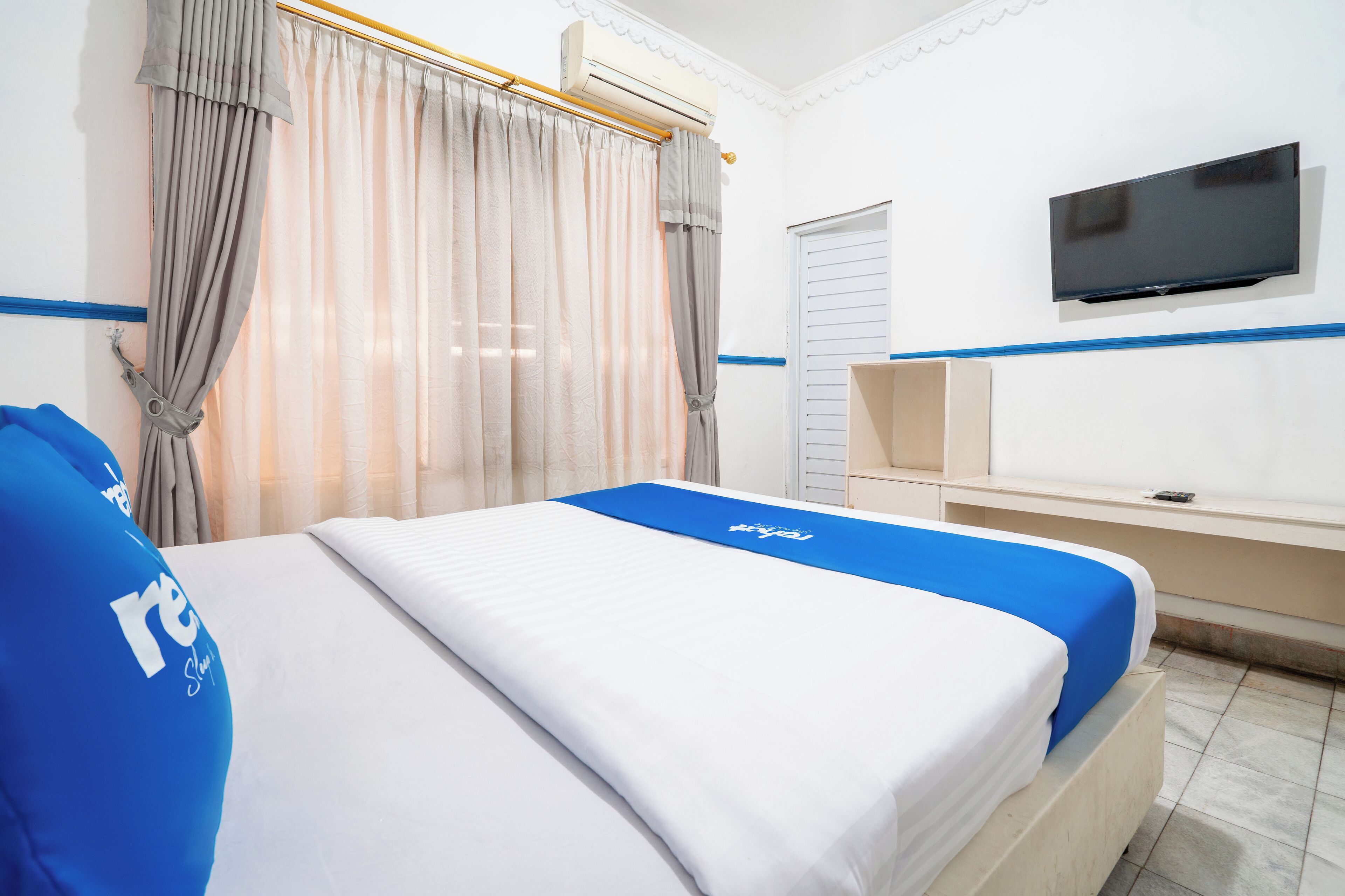 A hotel room with a bed, curtains, a TV, and a desk.