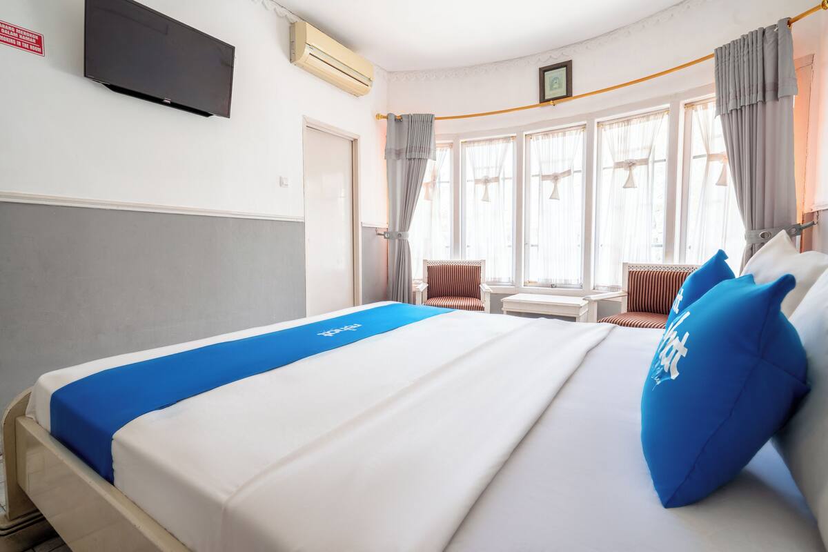 Ein Hotelzimmer mit einem Bett, einem Fernseher, einem Fenster mit Vorhängen, einem Sessel und einem kleinen Tisch.