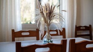A dining table with a clear glass vase containing dried pampas grass and small yellow flowers. - El Angel Vacation Home (Piñeres De Pria)