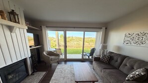 A living room with a fireplace, sofa, coffee table, and a view through a sliding glass door to an outdoor area. - 2026 Remodeled waterfront 1 bedroom escape on Lake Michigan in Glen Arbor MI (Glen Arbor)