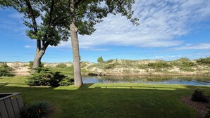 A grassy area with a pond, trees, and a wooden deck. - 2026 Remodeled waterfront 1 bedroom escape on Lake Michigan in Glen Arbor MI (Glen Arbor)