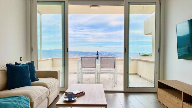 Un salon moderne avec un canapé, une table basse et une vue sur la plage grâce à de grandes portes coulissantes.