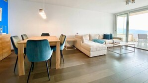Un salon moderne comprenant un coin repas, un ensemble de canapés et une grande fenêtre donnant sur un paysage agréable.