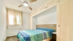 Une chambre à coucher avec un lit, un ventilateur de plafond, une fenêtre avec des rideaux et une armoire.