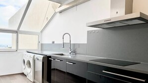 Une cuisine moderne équipée d’un lave-linge intégré, d’un évier en acier inoxydable et d’une grande fenêtre au-dessus du plan de travail.