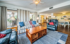 A spacious living room with a sofa, a leather armchair, a wooden coffee table, and a dining area in the background.