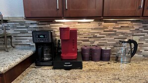 A kitchen with a coffee maker, a red coffee grinder, and three purple containers labeled coffee, tea, and utensils. - The Moonlight Express (Parker)