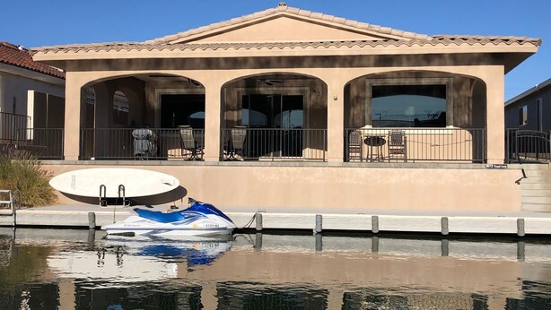 A Mediterranean-style building with a pool, outdoor seating, and a boat docked by the water. - The Moonlight Express (Parker)