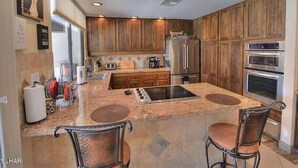 A kitchen with wooden cabinets, a central island with stools, a refrigerator, and an oven. - Kastle on the Keys, Private Dock (Parker)