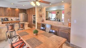 A modern kitchen with wooden cabinets, a dining area with a table and chairs, and a ceiling fan. - Kastle on the Keys, Private Dock (Parker)