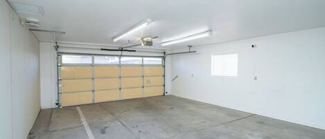 Un garage propre et dégagé, avec un sol en béton, une grande porte de garage, un éclairage fluorescent et un ventilateur de plafond.