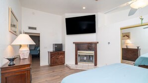 A hotel room with a bed, a television mounted on the wall, a fireplace, a wooden cabinet, and a lamp. - Oceans 11, Canal Front Family Fun, 60-FT Dock (Parker)