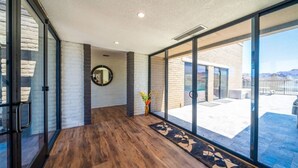 A spacious room with a wooden floor, large sliding glass doors leading to an outdoor patio, and a modern interior design with a white brick wall and a round mirror. - Eagles Lair, Pool & Views! (Parker)
