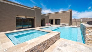 A modern outdoor pool area with two rectangular pools, a stone-tiled deck, and a brick building with large windows and a covered patio. - Eagles Lair, Pool & Views! (Parker)