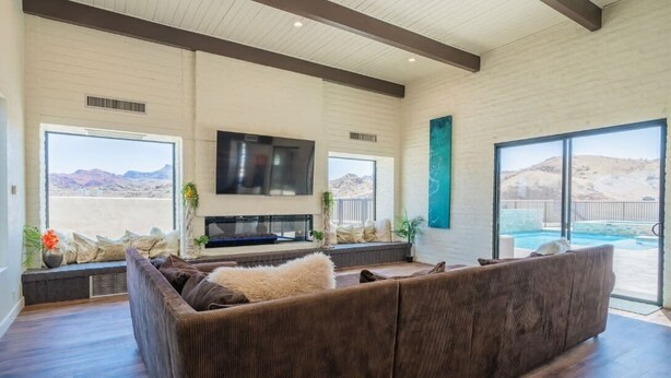 A spacious living room with a large sectional sofa, a flat-screen TV mounted on the wall, and a pool visible through the sliding glass doors. - Eagles Lair, Pool & Views! (Parker)