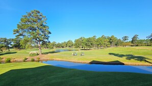 Un campo de golf con un estanque, árboles y un cielo azul despejado.