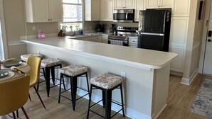 Una cocina moderna con armarios blancos, una isla central con taburetes, electrodomésticos de acero inoxidable y un ventanal grande.
