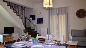 Un comedor con una mesa dispuesta para cuatro personas, una escalera, un televisor y un sofá.